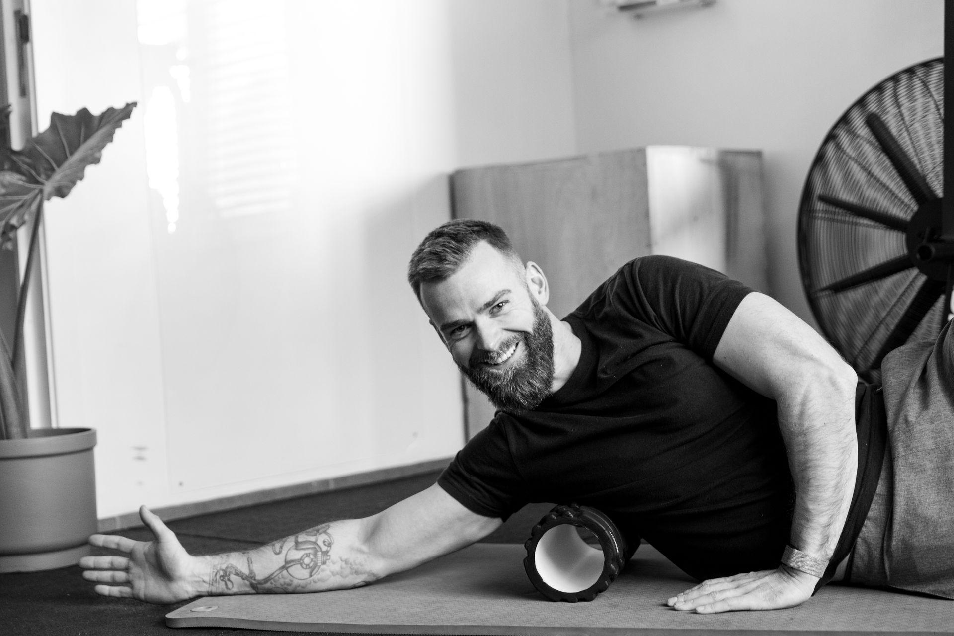 Man smiling while using a foam roller on his arm in a workout setting.