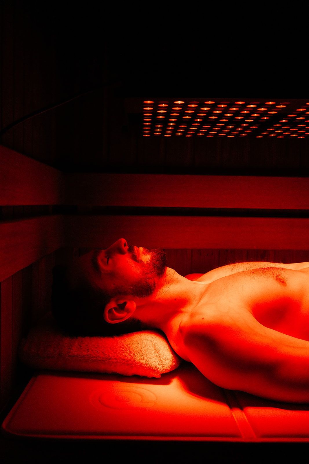 Person lying on a padded bed inside a sauna under the infrared red light therapy treatment.