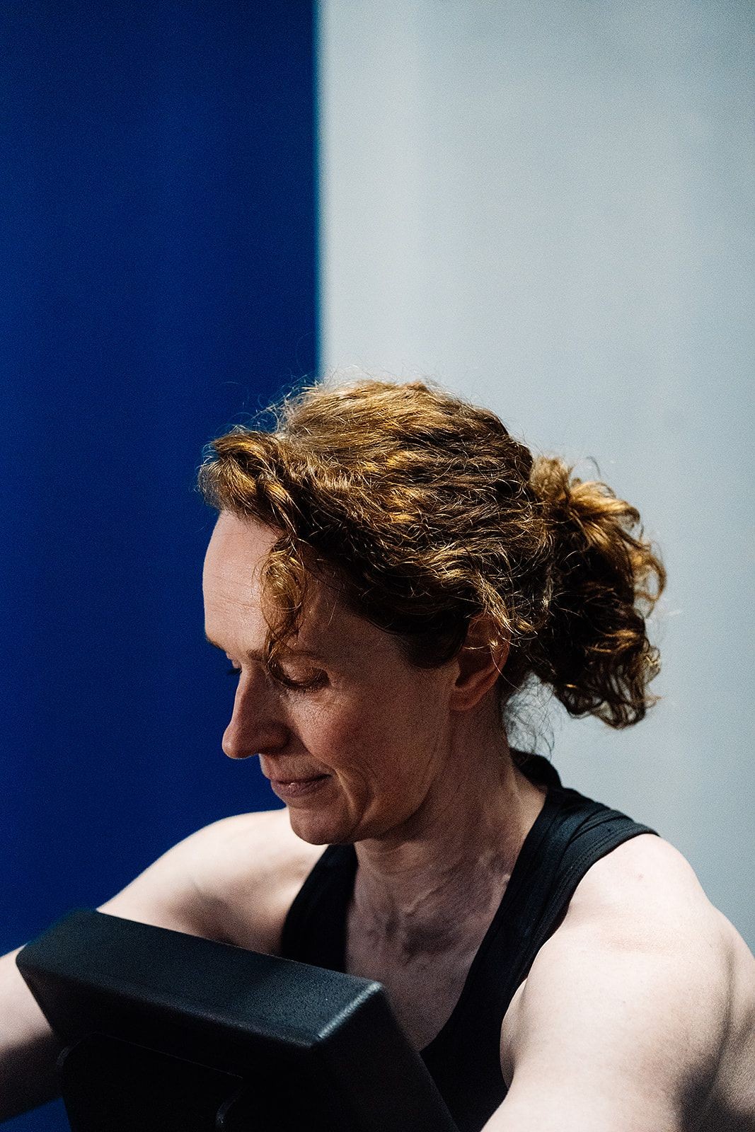 Person exercising on a stationary bike, wearing a black tank top, with curly hair tied back.